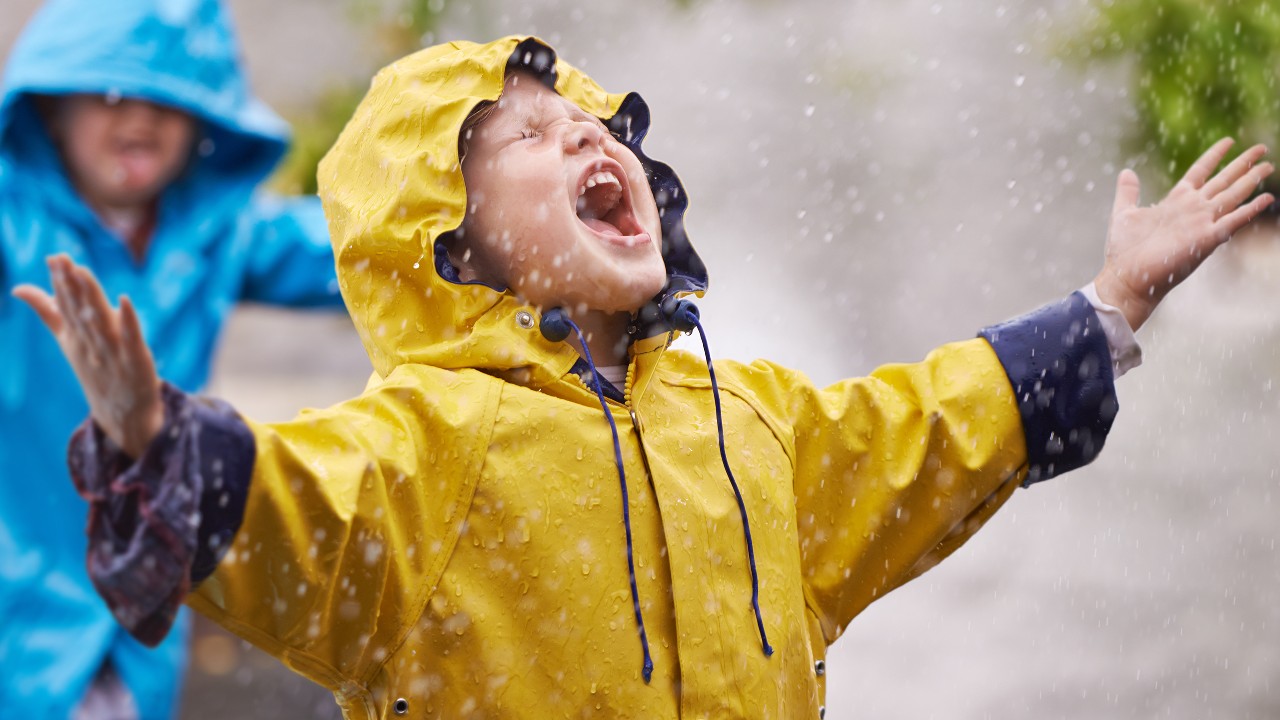 a kid enjoy the rain in a yellow raincoat